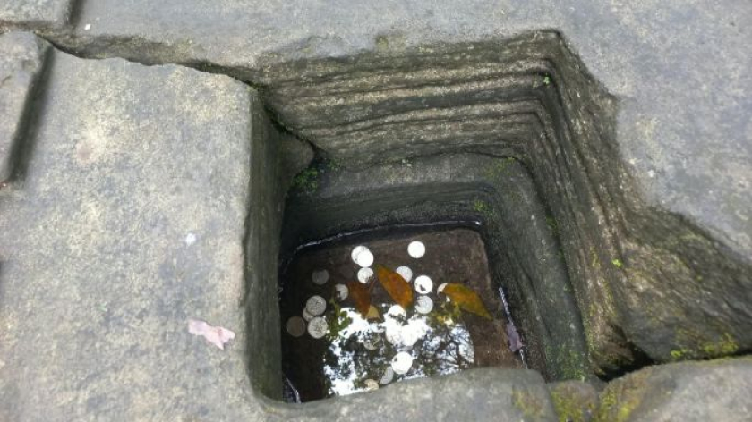 Koin di dalam genangan air di lubang Yoni batu balok persegi yang melambangkan Yoni. (Foto: Merrina Listiandari)