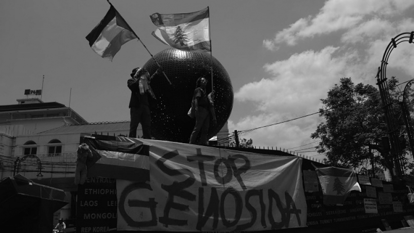 Aktivis dan seniman mengibarkan bendera Palestina mengacungkan poster di monumen Asia Afrika, Bandung, 7 Oktober 2024. (Foto: Prima Mulia/BandungBergerak)