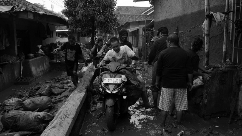 Warga membawa pakaian kotor naik sepeda motor pascabanjir bandang di Desa Banjaran Wetan, Kecamatan Banjaran, Kabupaten Bandung, 6 November 2024. (Foto: Prima Mulia/BandungBergerak)