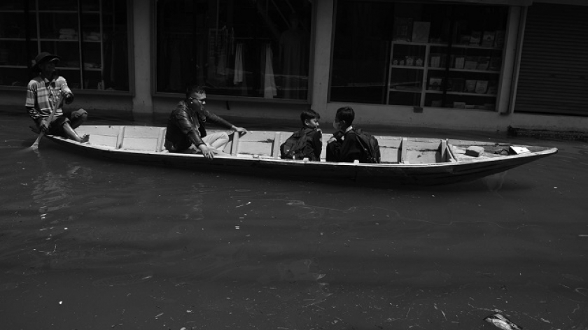 Warga naik perahu melewati toko-toko tutup di Cigebar, Kecamatan Bojongsoang, Kabupaten Bandung, 21 November 2024. (Foto: Prima Mulia/BandungBergerak)