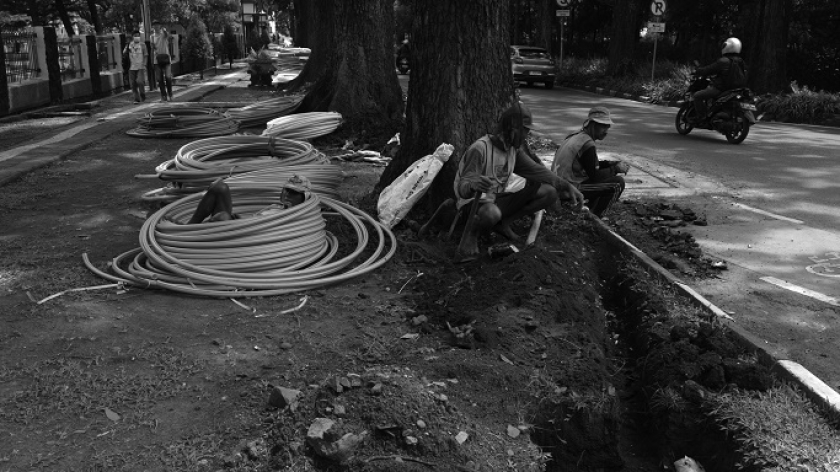 Proses pekerja memasukan pipa-pipa plastik ke dalam tanah di galian proyek ducting kabel serat optik Bandung bebas kabel udara di sejumlah ruas jalan protokol di Bandung, 10 Desember 2024. (Foto: Prima Mulia/BandungBergerak)