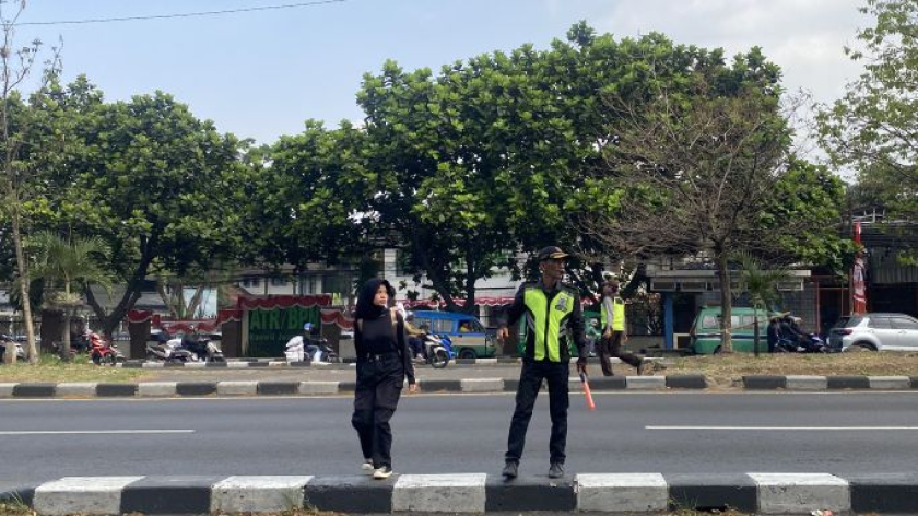 Satpam bertugas menyeberangkan anak sekolah di depan SMKN 9 Bandung Jalan Sukarno Hatta, Bandung, Agustus 2026. (Foto: Yopi Muharam/BandungBergerak)