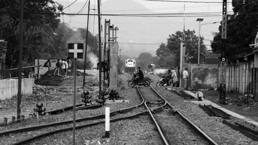 Kereta api dari Cicalengka menunggu giliran masuk ke Stasiun Haurpuguh, sementara beberapa warga menyeberang di perlintasannya, Minggu (14/11/2021) siang. (Foto: Prima Mulia/BandungBergerak.id)