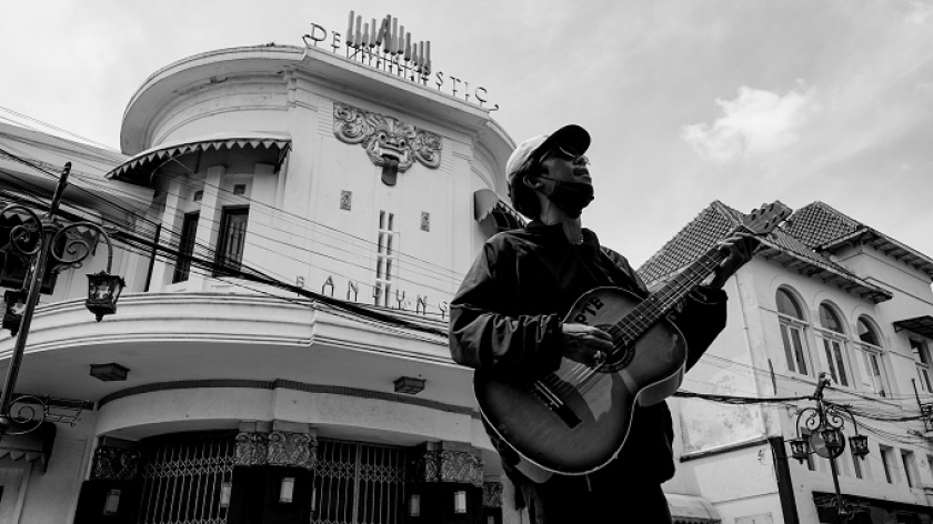 Seorang pengamen beraksi di seberang Gedung De Majestic, dulunya Asia Africa Cultural Center (AACC) yang kerap digunakan untuk aktivitas seni dan budaya, di Jalan Braga, Kota Bandung, Rabu (9/2/2022). Pada 9 Februari 2008 lalu di gedung ini terjadi insiden yang dikenal sebagai Sabtu Kelabu atau Tragedi AACC. (Foto: Virliya Putricantika/BandungBergerak.id)