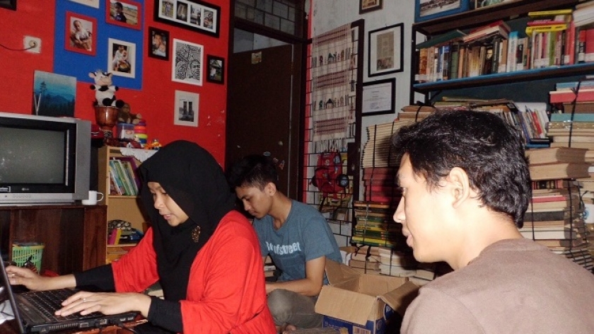 Suasana ruang tengah rumah penulis saat persiapan pameran. Gina (berbaju merah), Puji Ramdhani (berkaos abu-abu), dan Jiman Suhadi (membelakangi kamera). Area gudang di belakang foto sudah tak cukup menampung stok untuk untuk pameran. (Sumber: Deni Rachman)