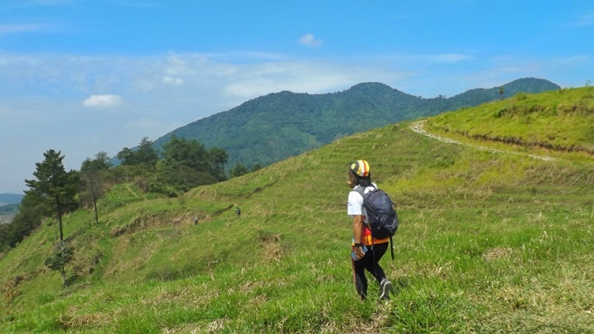 Seorang pendaki melintasi sabana atau padang rumput yang memukau di sekitar puncak Gunung Pangradinan, dengan penampakan Gunung Mandalawangi sebagai latarnya, Agustus 2022. (Foto: Gan Gan Jatnika)