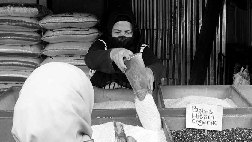 Elis (51 tahun) sedang melayani pembeli di kiosnya di Pasar Kosambi Bandung. Ia meneruskan usaha keluarganya berjualan beras untuk menghidupi dua anaknya. (Foto: Emi La Palau/BandungBergerak.id)