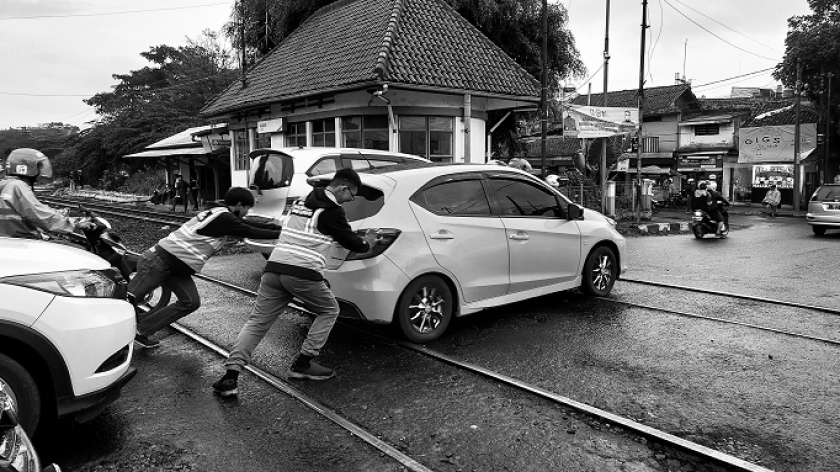 Dua anggota Edan Sepur membantu mobil yang tergelincir di besi perlintasan kereta yang licin, di Jl. Garuda, Sabtu (25/2/2023). (Foto: Awla Rajul/BandungBergerak.id)